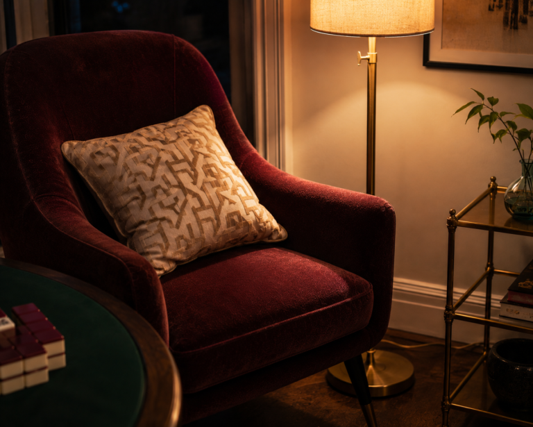 A burgundy velvet chair and brass floor lamp styled beside a mahjong table.
