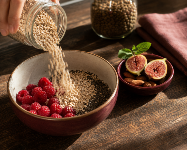 How much fiber do you need daily — a hand pouring oats into a bowl of raspberries and chia seeds in morning light.