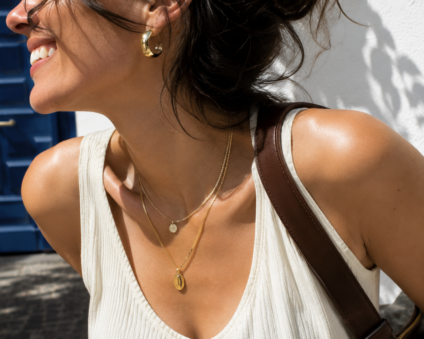 Woman mid-turn in bright daylight wearing layered necklaces and an earring — an example of everyday jewelry that doesn't tarnish, shown in natural motion rather than a close-up product shot.